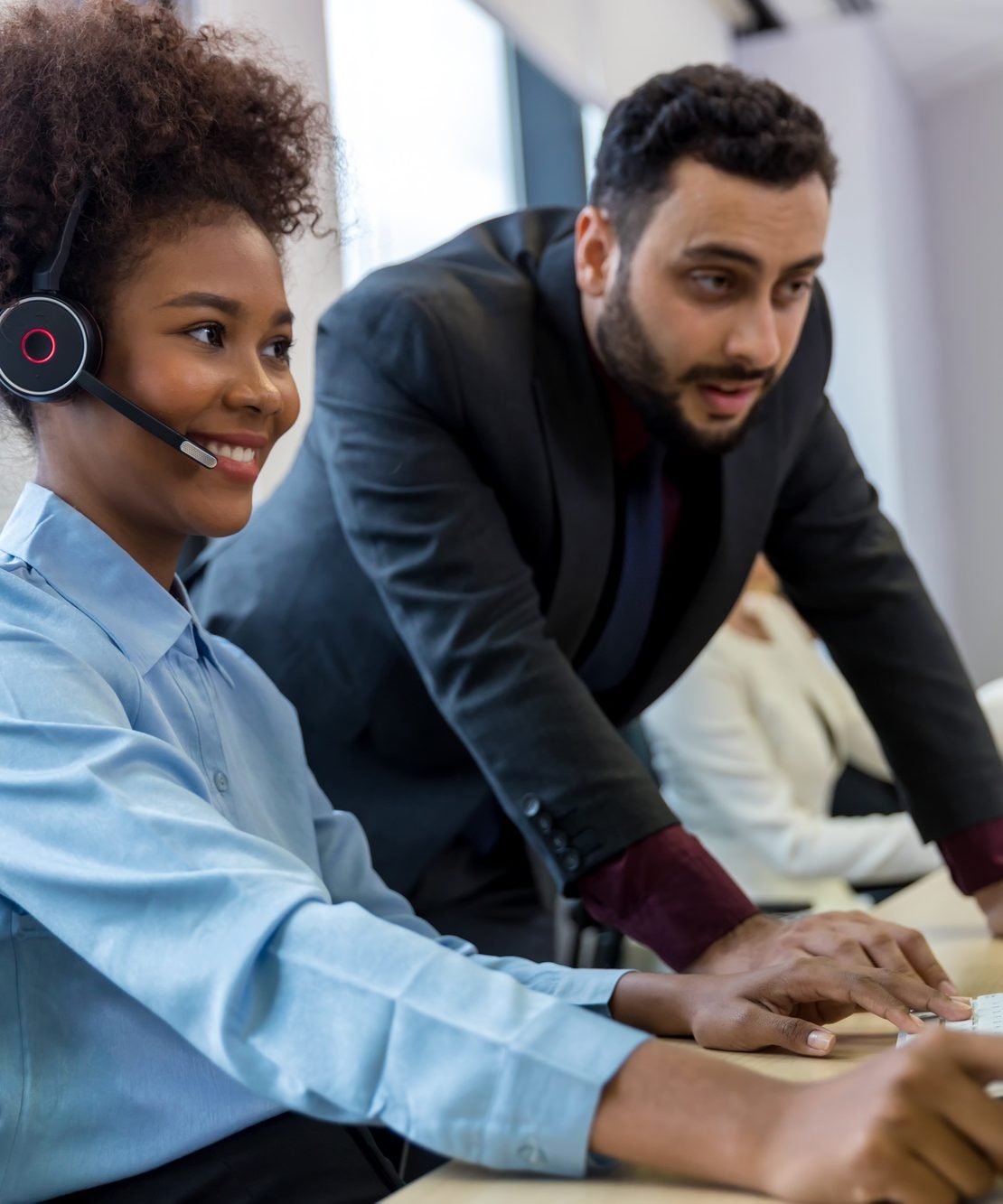Call center business woman talking on headset. Call center worker accompanied by her team.